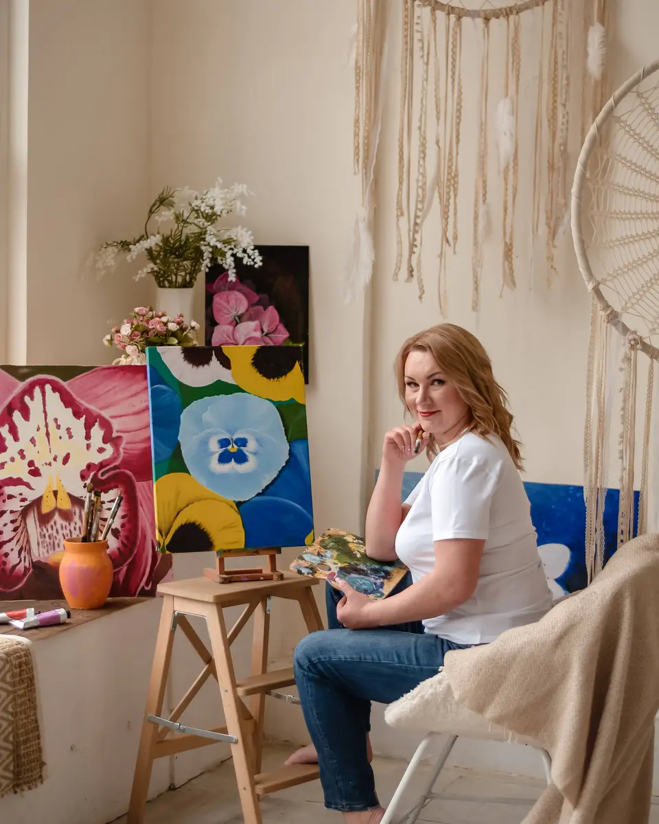 Юлія Сатир у своїй студії біля мольберта з квітковою картиною